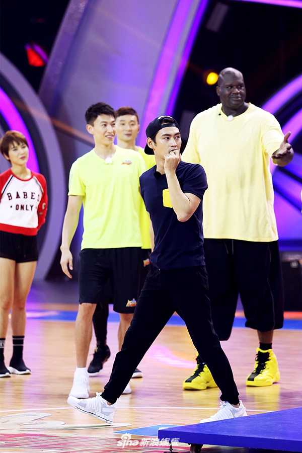 大鲨鱼空降中国赛场刘炜刘晓宇携手奥尼尔上演综艺篮球嘉年华 郑恺站在奥尼尔身边试图干扰其投篮,两人身高对比悬殊,但郑恺表情认真投入,画面充满竞技游戏的趣味