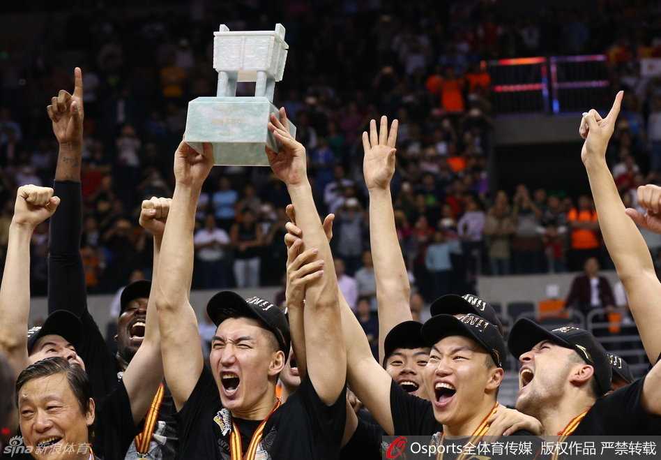 新疆队的全体将士身穿冠军T恤，共同托举起那尊象征着最高荣誉的CBA总冠军奖杯，大家紧紧靠在一起，笑容定格在这一历史瞬间，画面充满了团结与喜悦。