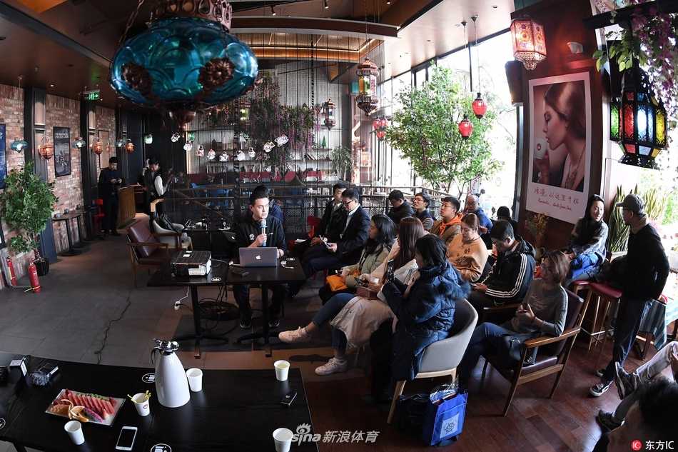 活动现场大屏幕上正在播放CBA比赛录像，画面定格在一次争议判罚的瞬间，两名裁判手持教鞭指向屏幕，向台下媒体进行讲解。