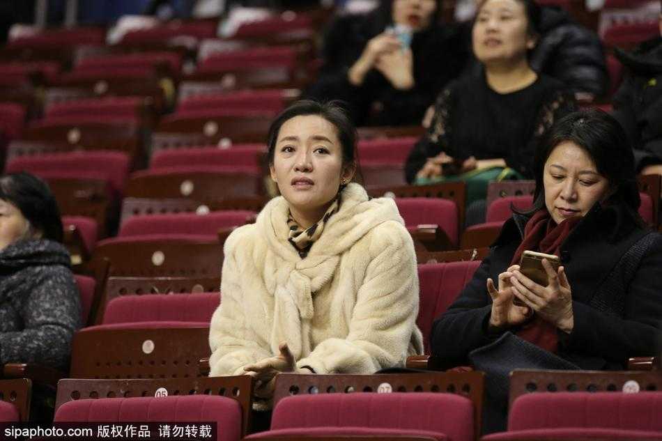 赛场边，一对情侣球迷依偎而坐，两人身上华贵的貂绒在灯光下泛起柔和光泽，男生正指向场内的记分牌，脸上露出轻松的笑容。