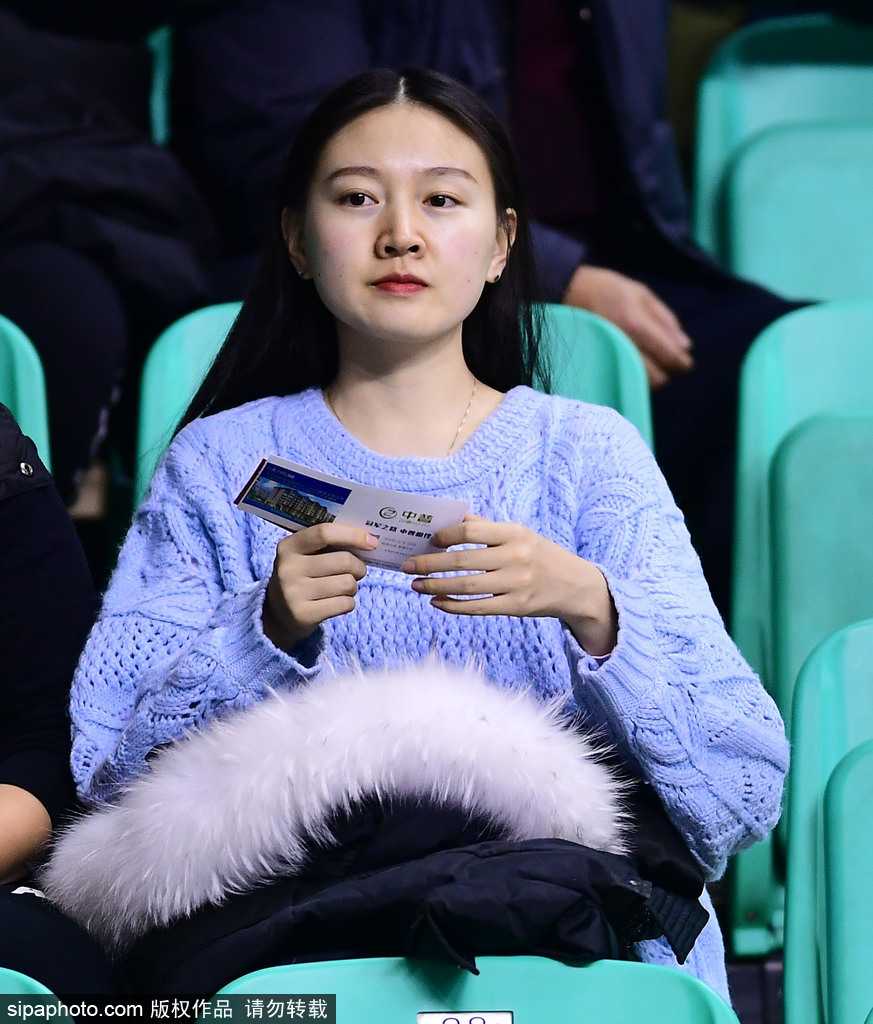 这名戴着黑框眼镜、气质文静的女生在人群中显得格外特别，她侧身倚靠在看台栏杆上，手中紧握着助威棒，嘴角带着一丝若有若无的微笑，仿佛在沉思，又仿佛在享受比赛间隙的片刻宁静。