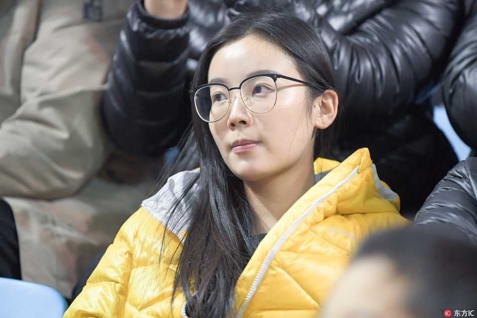 一位穿着时尚牛仔外套的甜美女生，双手轻轻放在膝盖上，脸上露出纯真而灿烂的笑容，显然是被现场热烈的气氛所感染。