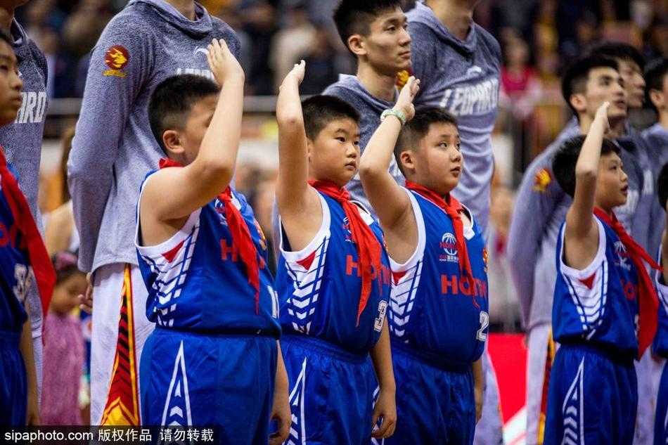 身穿白色球衣的稚嫩篮球少年，在热烈的赛场氛围中，双手紧握篮球，眼神坚定地望向场内，仿佛下一秒就要上场冲锋陷阵。