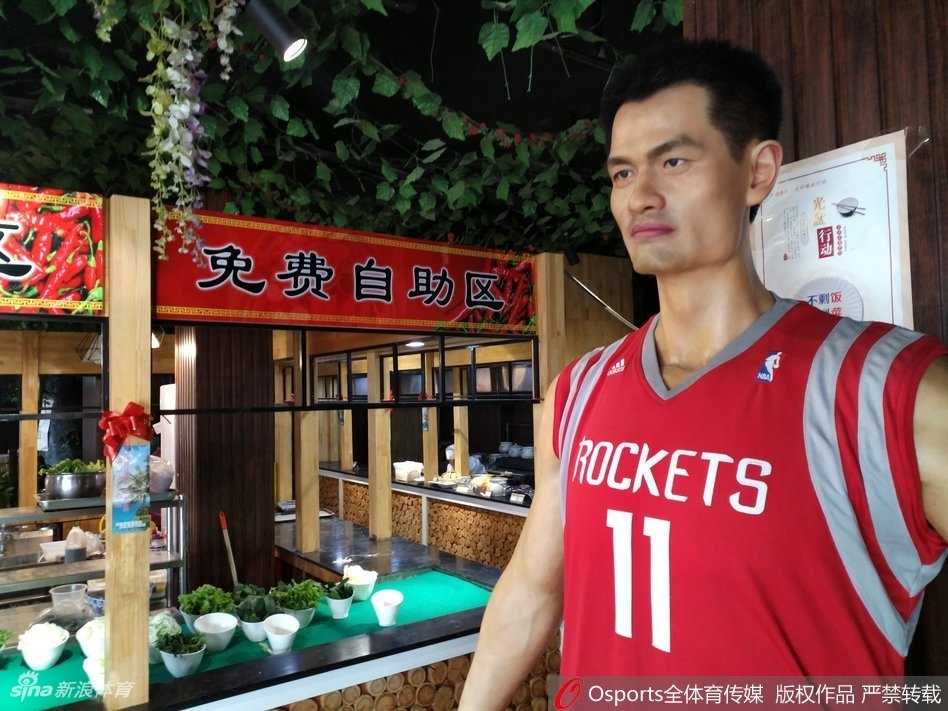 食客们正在排队与蜡像合影留念，一名小男孩好奇地伸手想触碰蜡像的球衣，脸上洋溢着兴奋的笑容，现场氛围欢乐融洽