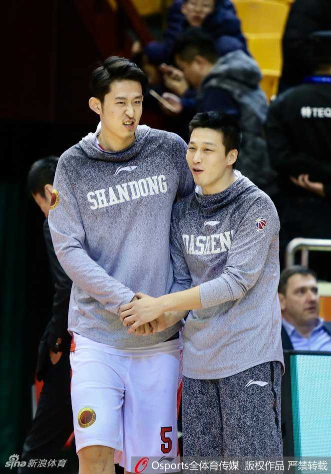 队友正在进行拉伸训练，一旁的丁彦雨航忍不住搞怪，用皮球干扰，队友则露出无奈又开心的笑容。