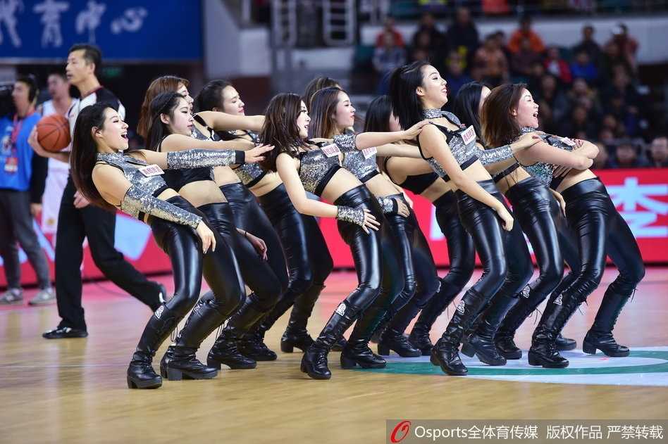 多名篮球宝贝背对镜头，面对看台上热情的球迷，她们高举双手做出富有感染力的指挥动作，黑色的皮裤在球场灯光下质感十足，带领全场观众掀起一波又一波的人浪。