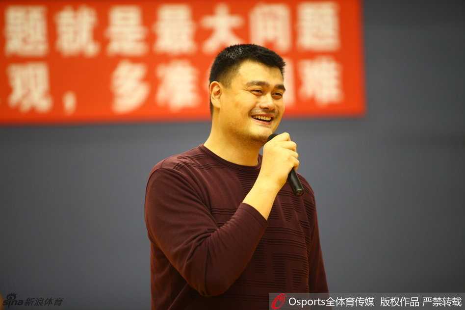 篮球巨人姚明面带标志性微笑，微微俯身与一群满脸稚气却眼神热切的国少队小球员击掌互动，巨大的身高差构成了一幅关于传承与梦想的动人画面。