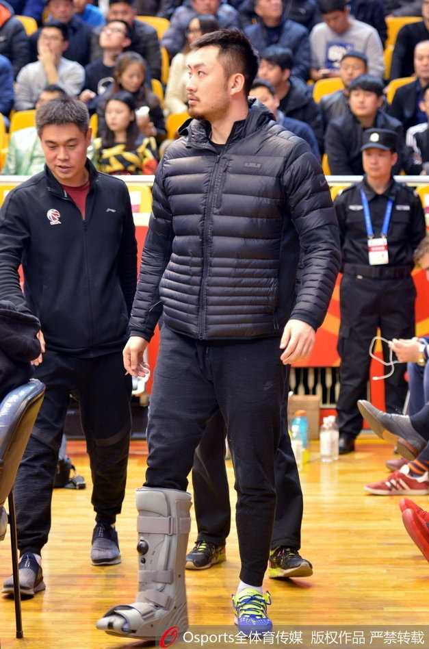 睢冉在场边专注地看着比赛，他的侧脸线条硬朗，下巴上蓄着标志性的胡须，身后的看台上坐满了热情的山东球迷，大家的目光都聚焦在场上，而睢冉的脚伤让他只能静静地坐着。