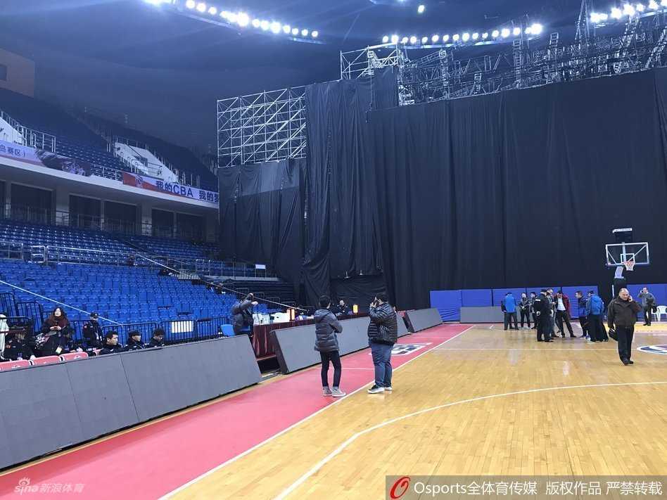 当篮球架遇见演唱会舞台:一场因“跨界”而取消的CBA比赛 空旷的青岛国信体育馆内,一座为跨年晚会搭建的钢铁舞台占据了篮球场北侧,舞台的金属桁架与篮球架并立,体育馆顶部的灯光照射在场地上,形成了一种比赛与演出交织的奇异景象。