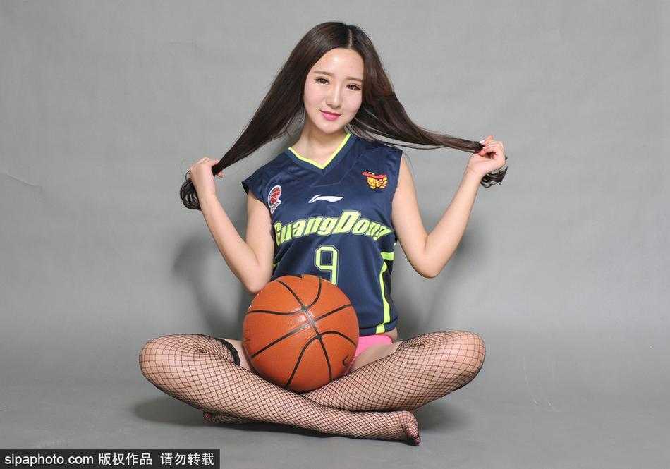 镜头聚焦在宝贝纤细的脚踝和脚下的篮球鞋上，黑色的丝袜在球场灯光下泛着微光，她身体微曲，双手指尖比出爱心，将赛场边的铁马变成了展示美丽的舞台。