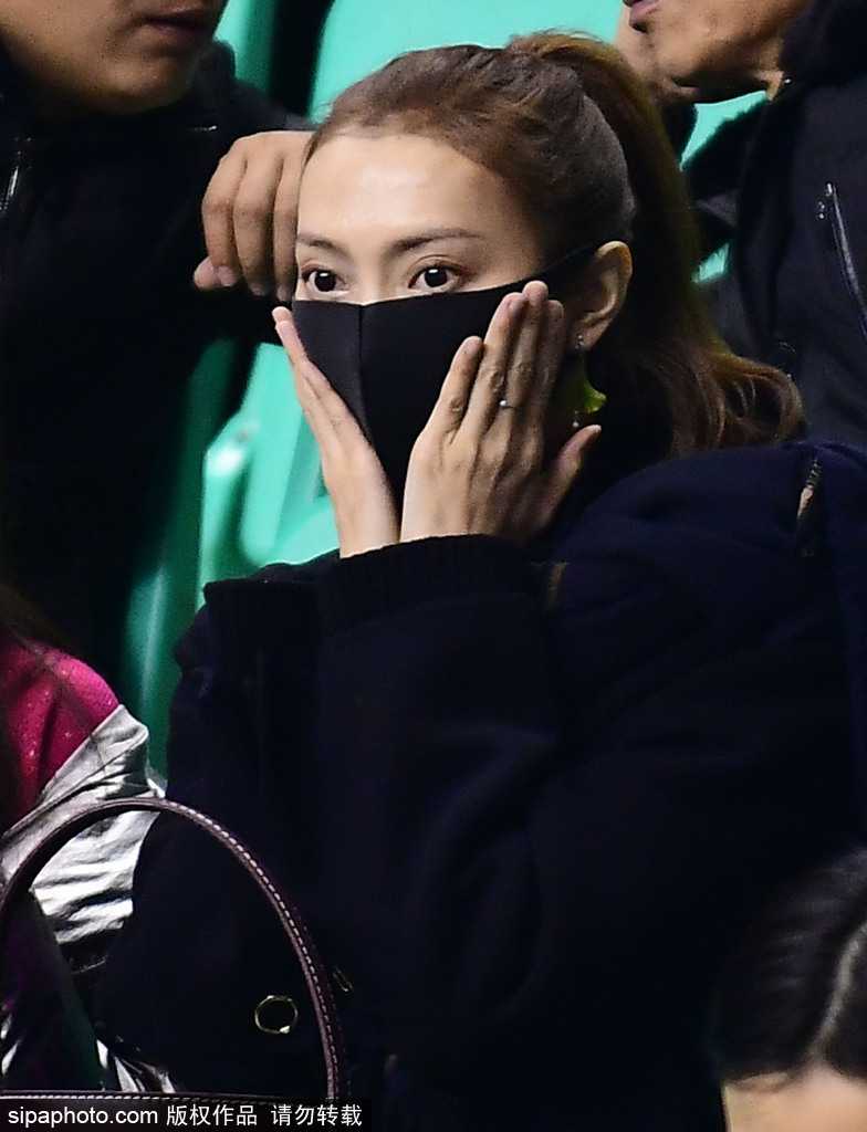 李旭在人群中回眸一笑，面容精致清秀，她身着一袭时尚外套，在喧嚣的球场看台上显得格外亮眼夺目。