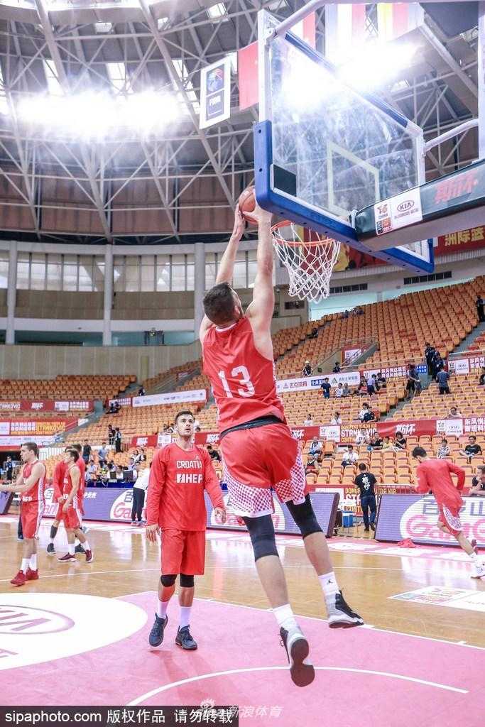 克罗地亚队球员在深圳体育馆进行赛前热身，他眼神专注，高高跃起试图封堵队友的投篮，场馆顶棚的灯光映照在球员们汗水闪烁的肩膀上，大战前夕的紧张感在空气中弥漫。