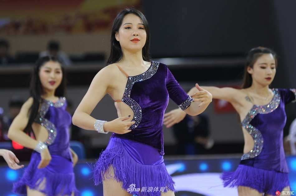 一名笑容甜美的啦啦宝贝在聚光灯下完成了一个高难度的托举动作，她手中金色的花球在空中划出优美的弧线，仿佛将体育馆的上空都染上了青春的色彩。