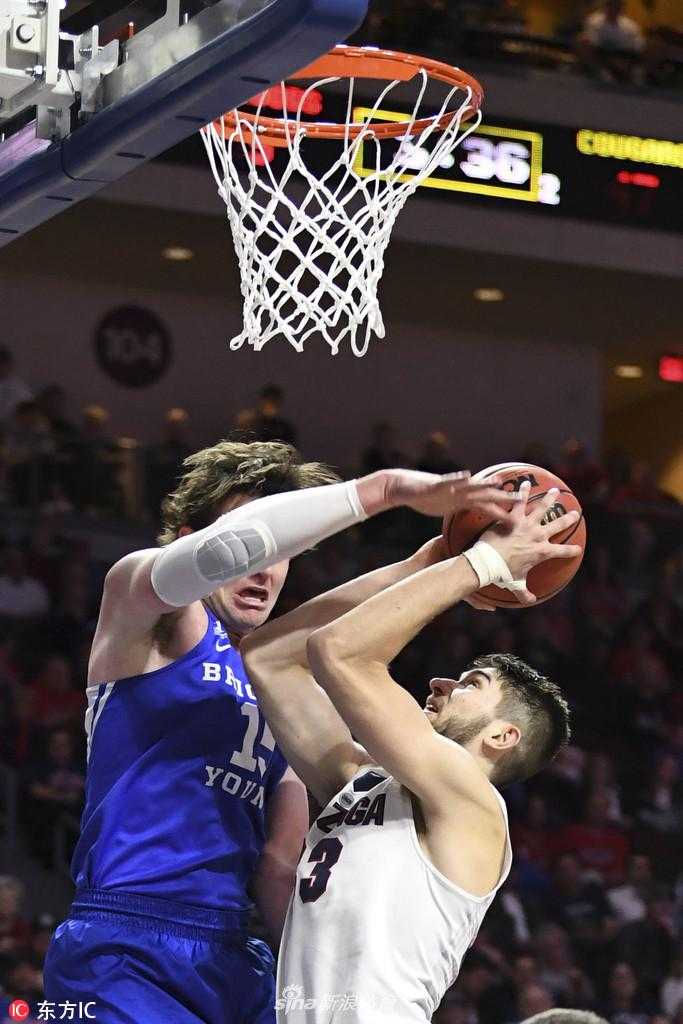 杨百翰大学的核心球员约埃尔·查尔德在巨人丛林中强行上篮。他的身体在空中完全舒展，肌肉线条因为发力而紧绷，面对冈萨加两名防守球员的遮天蔽日，他眼中没有丝毫畏惧，只有对篮筐的无限渴望。这一球，是他全场战斗精神的一个缩影。