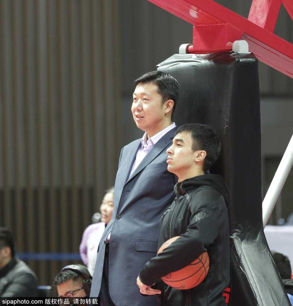 大郅侧身而立，仿佛与身边的好友低声交流着场上的局势，嘴角挂着一丝淡淡的微笑，那笑容里饱含着对篮球纯粹的爱与对后辈的无限包容。