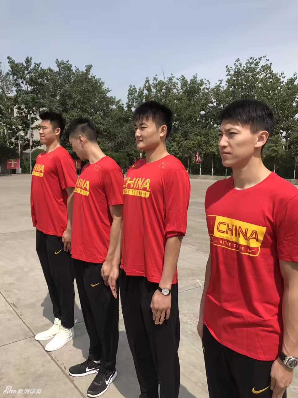 空旷的训练场上，男篮队员们整齐列队，在教官的口令声中反复练习转身与敬礼。远处的训练标语在烈日下泛着光，身影被拉得修长，这一刻的汗水与坚持，将成为他们日后在赛场上拼搏的宝贵精神财富。