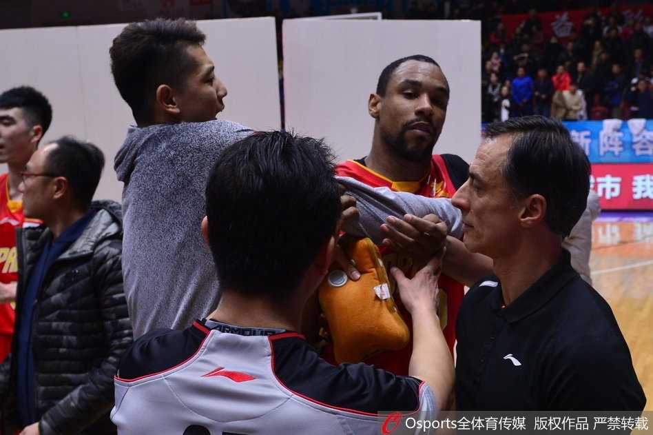 从侧面看去，萨林杰被围堵在人群中，他的眼神死死盯着新疆队球员离开的方向，双臂被队友紧紧锁住，肌肉紧绷，仿佛下一秒就要挣脱束缚。