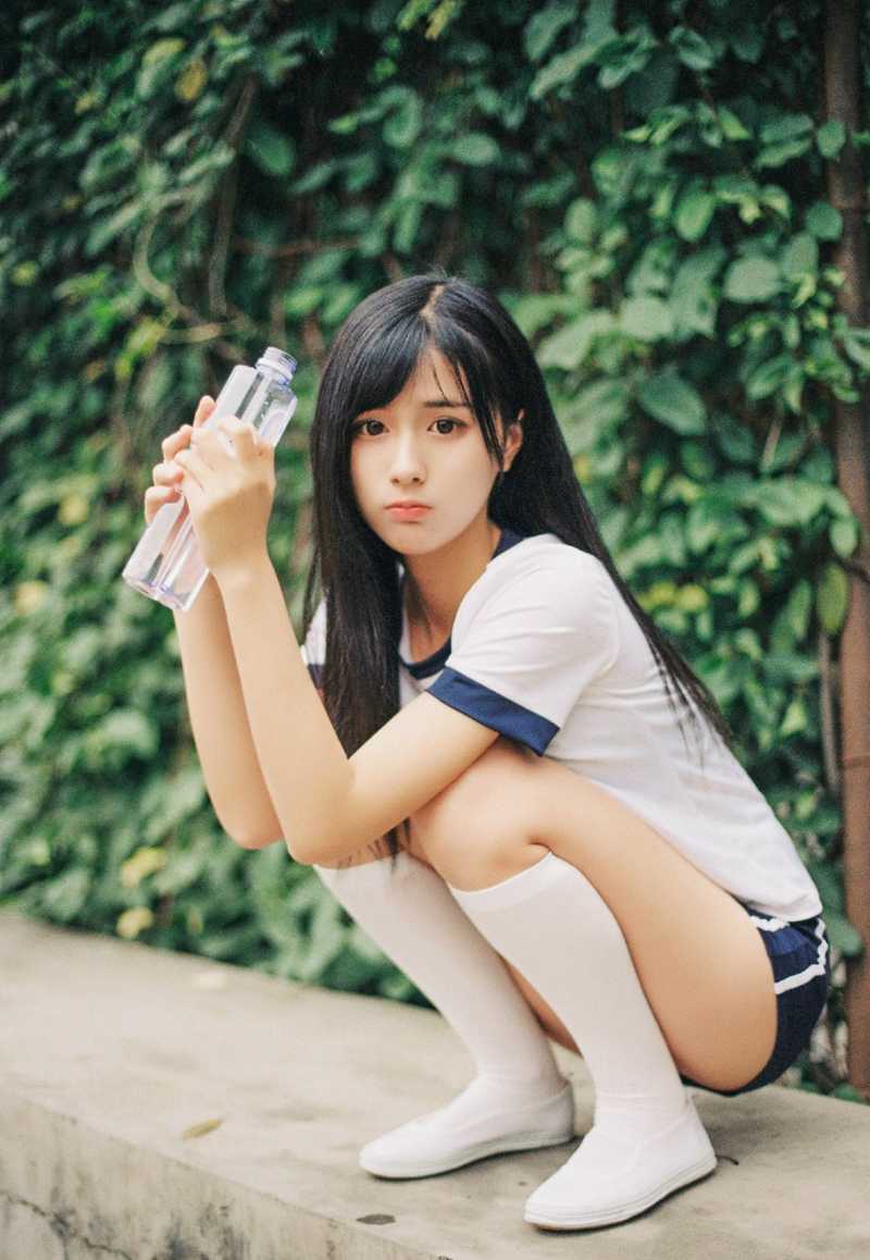 她双手轻托脸颊，眼中映出绿色草坪的光影，嘴角带着少女般俏皮的笑意，青春气息扑面而来。