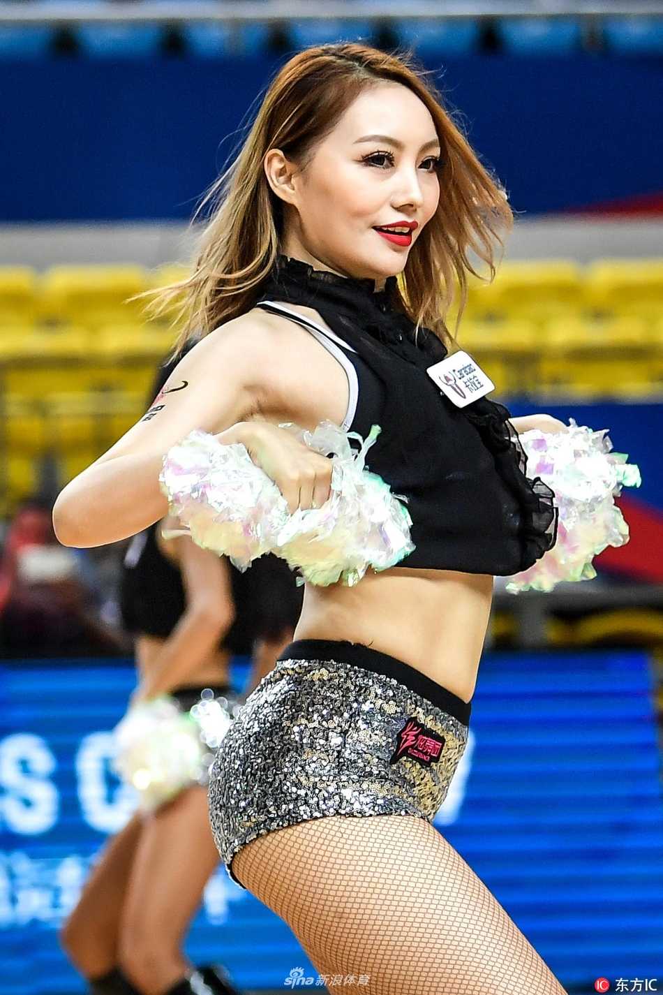 领舞的宝贝面带甜美微笑，双手随着音乐节奏有力挥舞，身后的队友们动作整齐划一，她们与背景板上激烈的赛事logo相映成趣，构成一幅力与美的画卷。