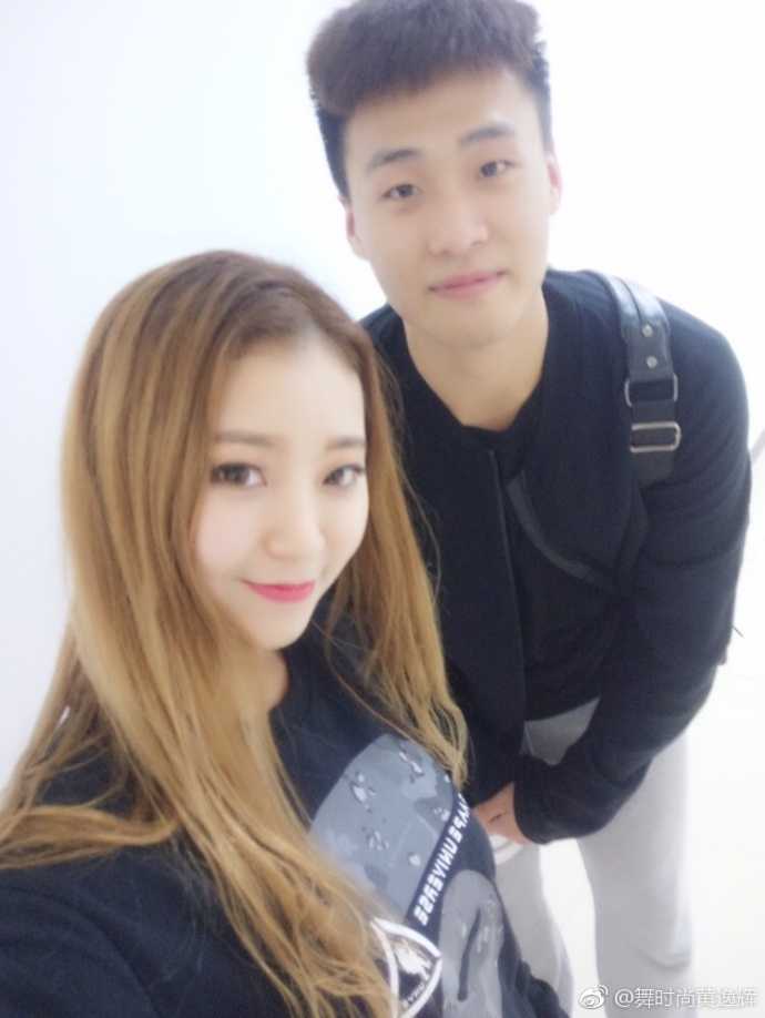 黄逸辉被几位宏远队的小鲜肉环绕在中间，她开心地对着镜头比心，身后是球员们略带青涩的笑容，画面充满活力。