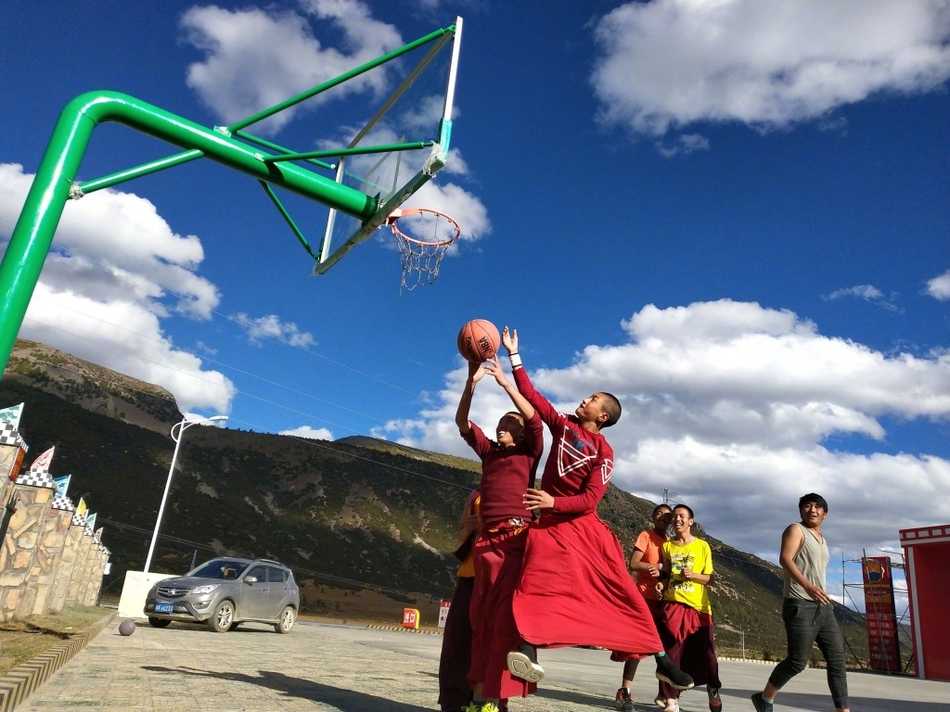 红尘之外的篮球梦,稻城蚌普寺僧袍下的灵动身影 在高原湛蓝的天空下,一位身着绛红僧袍的喇嘛高高跃起,手中的篮球仿佛要挣脱地心引力,他的身影在简陋的篮球架前显得格外轻盈而专注。