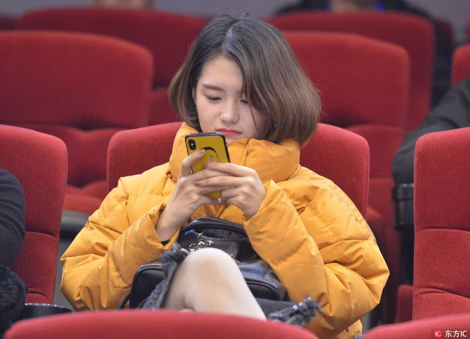 一位身着深色外套的短发女球迷，在微暗的看台上嘟嘴卖萌，神情俏皮可爱，与身后紧张观赛的人群形成鲜明对比。