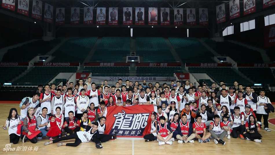 训练间隙，一名广州男篮球员弯下腰为蹲在地上的小球迷在篮球上签名，周围站满了其他等待签名的热情球迷，场面十分有爱。