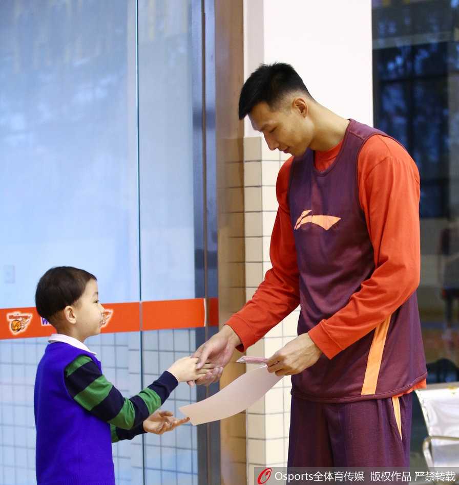 轩轩手持签名篮球，与身穿训练服的广东宏远队员面对面交流，队员俯身倾听轩轩说话，画面温馨感人。