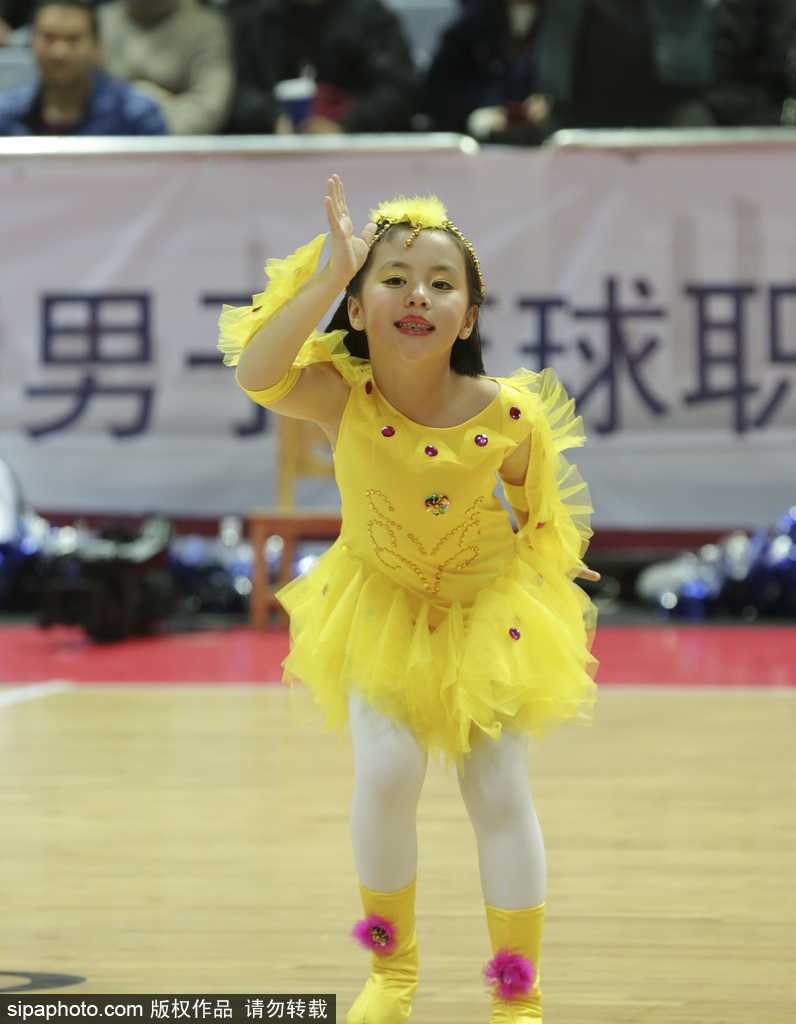 侧拍镜头下，一名萌娃啦啦队员高高举起手中的彩球，仰头看向空中的花球，眼神中充满好奇与星光，上扬的嘴角透露出表演带来的纯粹快乐。