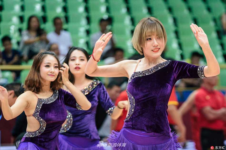 一名篮球宝贝在聚光灯下展现柔美身姿，她轻轻扭动腰肢，双手优雅伸展，仿佛一朵在赛场边盛放的铿锵玫瑰，与身后激烈的计分牌形成一动一静的巧妙对比。