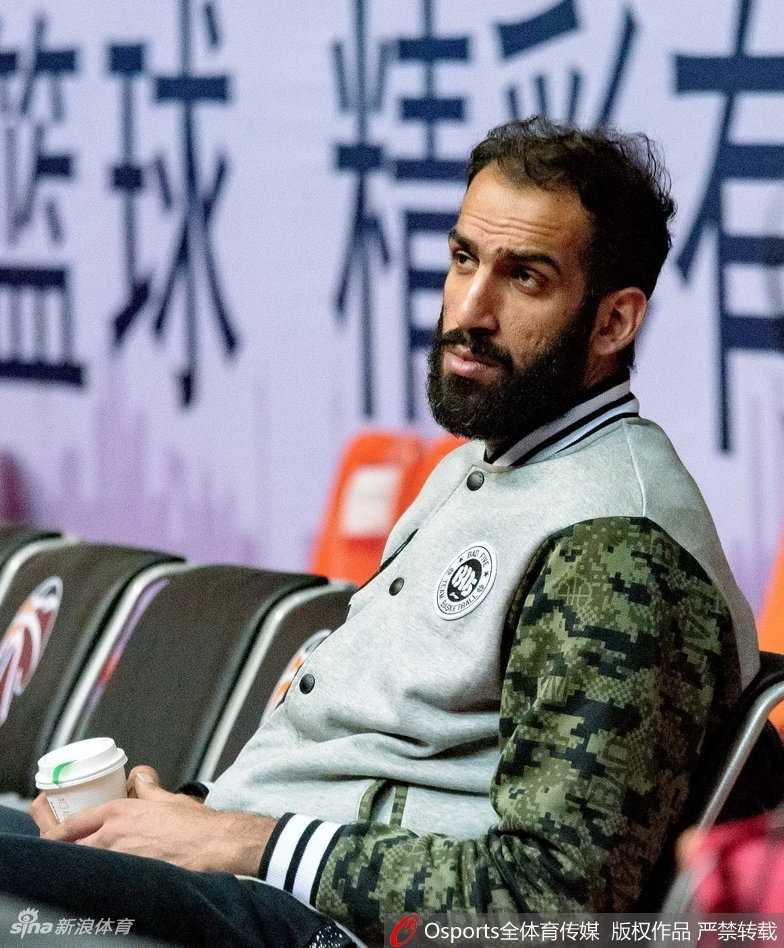 哈达迪与队友在场边交流，他紧握冒着热气的杯子，身旁的年轻球员认真聆听这位老大哥的指点。