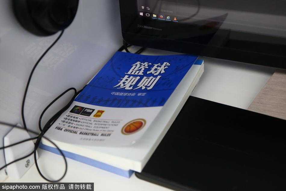 一位经验丰富的值班裁判神情专注，他面前的屏幕定格在一次激烈的篮下对抗瞬间，他正在通过耳麦与现场裁判进行沟通。