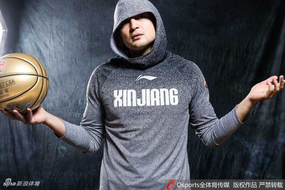 西热力江的嘻哈战袍:新疆后卫的霸气写真与揭幕战传奇 西热力江半身肖像,身穿浅色帽衫,头戴黑色毛线帽,身后是斑驳的墙壁,整体风格简约却极具嘻哈街头感