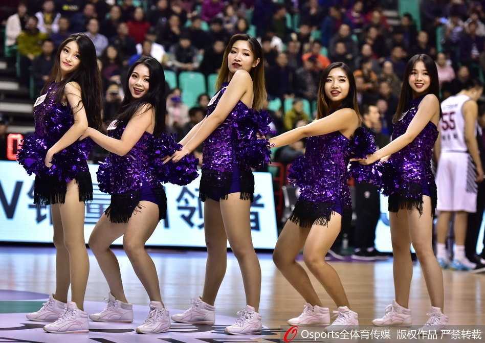 一位啦啦队员在聚光灯下优雅转身，裙摆轻扬间露出修长笔直的双腿，展现出力量与柔美并存的舞姿。