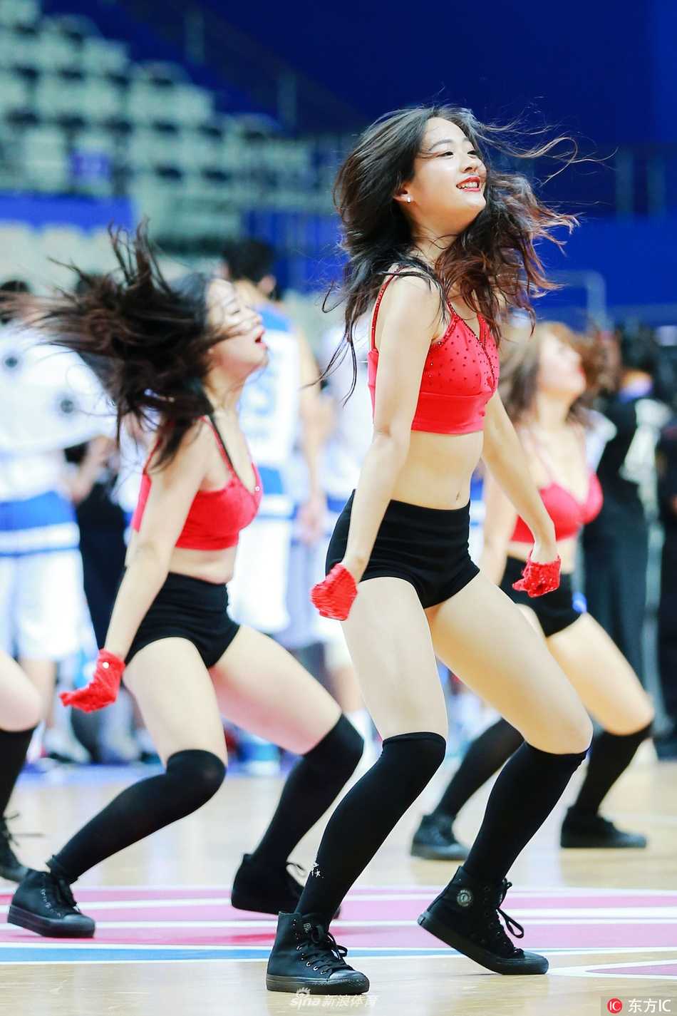 镜头捕捉到一位正在准备中的拉拉队宝贝，她赤足静立，目光望向远方，匀称的双腿线条和简约的队服相得益彰，仿佛在用无声的语言为即将开始的比赛积蓄能量。