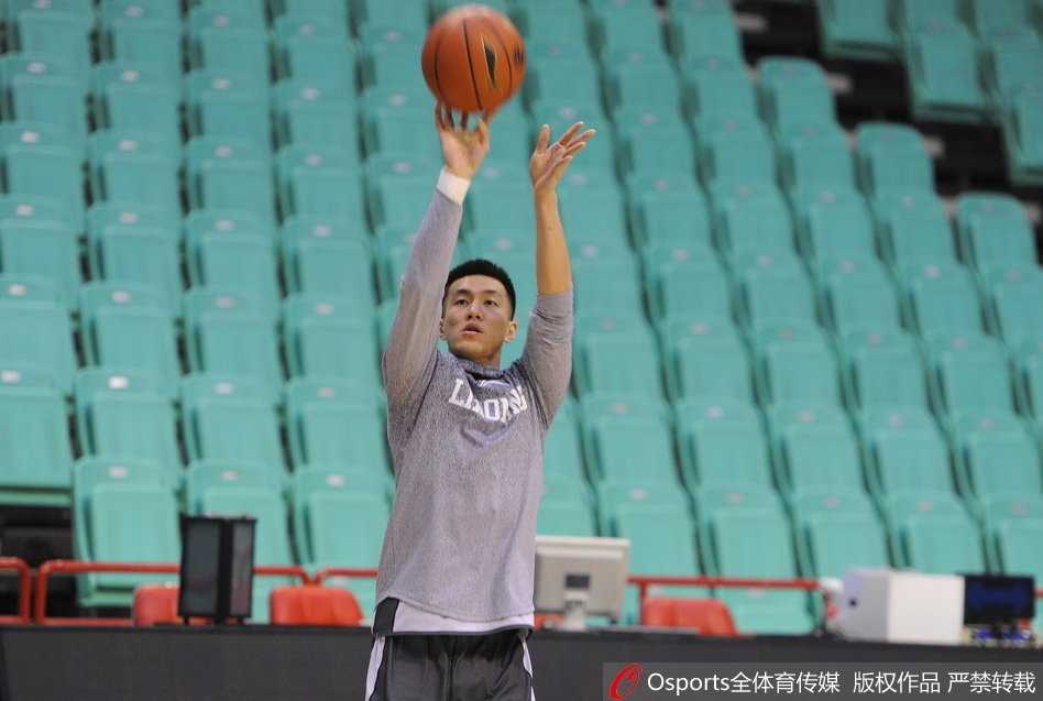 巴斯妻子抱着儿子站在场边，一家三口其乐融融，背景是训练中的辽宁队