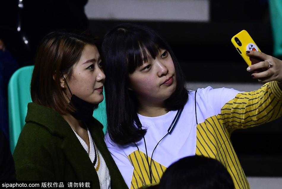 在人群的缝隙中，另一位留着齐刘海的清秀女球迷被捕捉到了镜头。她身着浅色上衣，安静地坐在座位上，即使周围是狂热的球迷，她依然保持着温婉的神情，如同喧嚣中的一股清流，静静地欣赏着这场篮球盛宴。