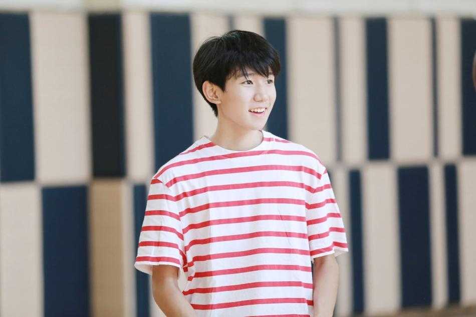 王源在球场中央舒展身体如飞鸟展翅，红色条纹衫下摆扬起，黑色运动裤与背景的绿茵形成鲜明对比，定格青春最美的剪影