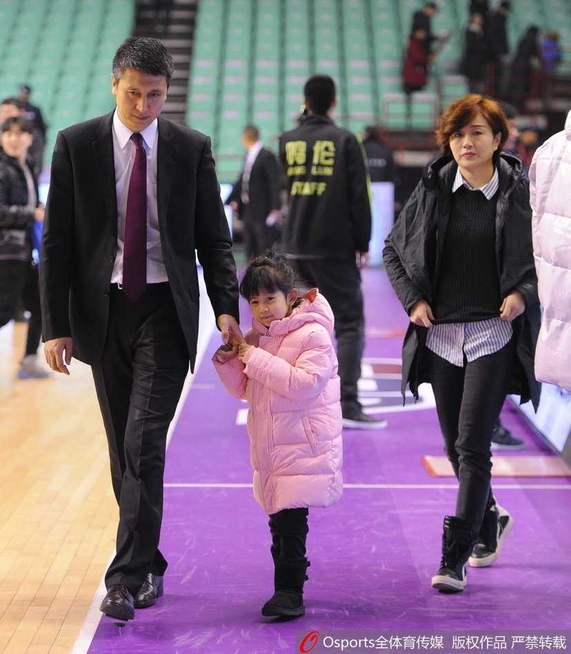 郭士强指导身披蓝色长款羽绒服，眼神温柔地低头看着身旁的女儿，小姑娘则紧紧牵着父亲的手，父女俩在众人的陪同下离开赛场，画面温馨极了。