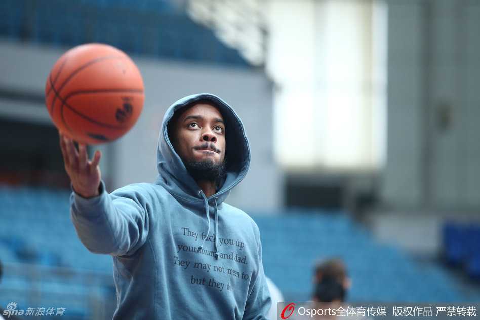 身披休闲帽衫的杰伦-布朗坐在场边休整，目光如炬地瞄准远处篮筐，放松姿态中难掩专注杀气