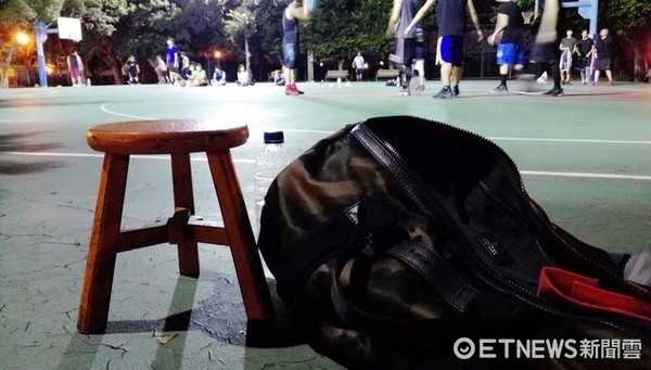 鏡頭拉近，蕭敬騰專注地看著場上的比賽，手裡拿著毛巾。他身後那張古樸的木頭板凳，在這個現代化的球場上顯得格外搶眼，仿佛在訴說著一位巨星回歸質樸、熱愛運動的初心。