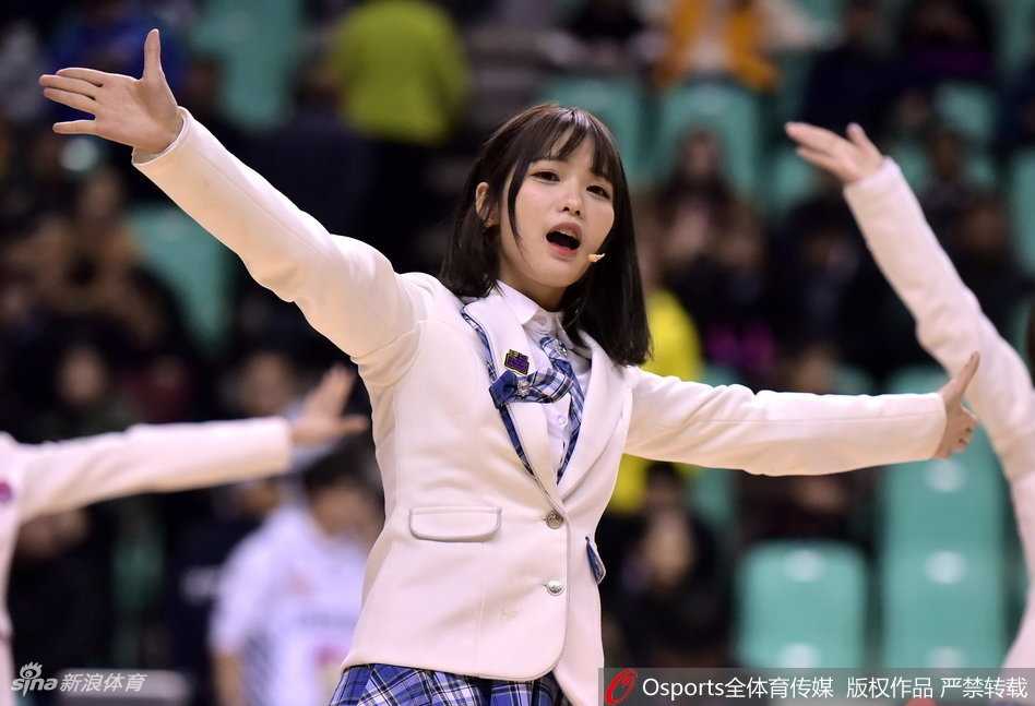 SHY48成员以体育馆大屏幕为背景摆出可爱的加油手势，身后是热烈的比赛现场，她们的笑容与场馆内的灯光交相辉映。