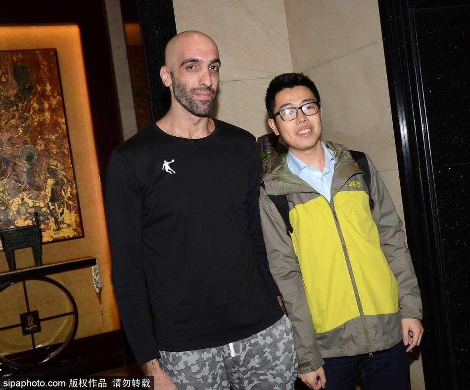 画面中是马布里的一个侧影，他正在为球迷手中的球衣签名，背景是虚化的酒店大堂。灯光打在他花白的胡子上，诉说着岁月的沉淀与不变的坚守。