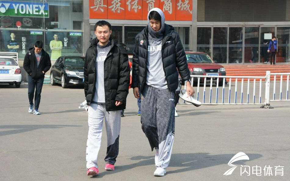 山东男篮训练场上，助理教练正拉着一位眼神专注的年轻球员进行挡拆战术的拆解讲解，小伙子额头上的汗珠在灯光下闪闪发亮，手中的篮球仿佛承载着季后赛的希望。