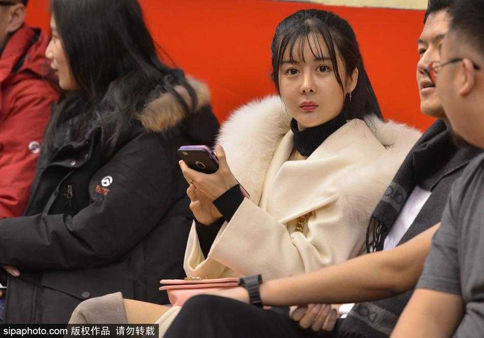 一位戴着眼镜、文静秀气的女球迷，双手轻轻放在身前，脸上洋溢着满足而温暖的微笑，在这充满对抗的球馆里，如同一阵和煦的春风。