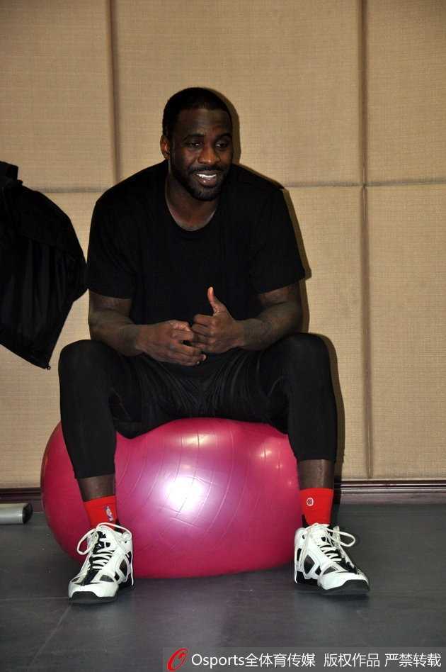 训练馆内灯火通明，泰·劳森身披山东高速战袍，刚刚归队的他与丁彦雨航并肩坐在场边的广告牌上，两人相视而笑，丁彦雨航一边比划一边说着什么，劳森则认真倾听，眼神中满是默契与坚定。